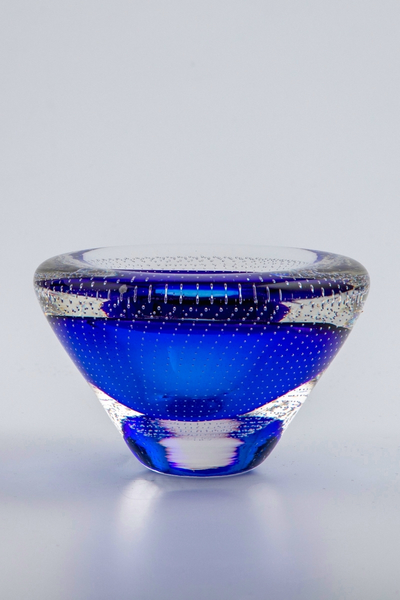 Vase i underfangsglass. Konisk form med et blått sjikt rundt munningen, omgitt av en klar glassmasse. Konkavt toppstykke med liten sirkulær åpning. Korpus er dekorert med små radiale luftbobler som er innlagt i glassmassen.
