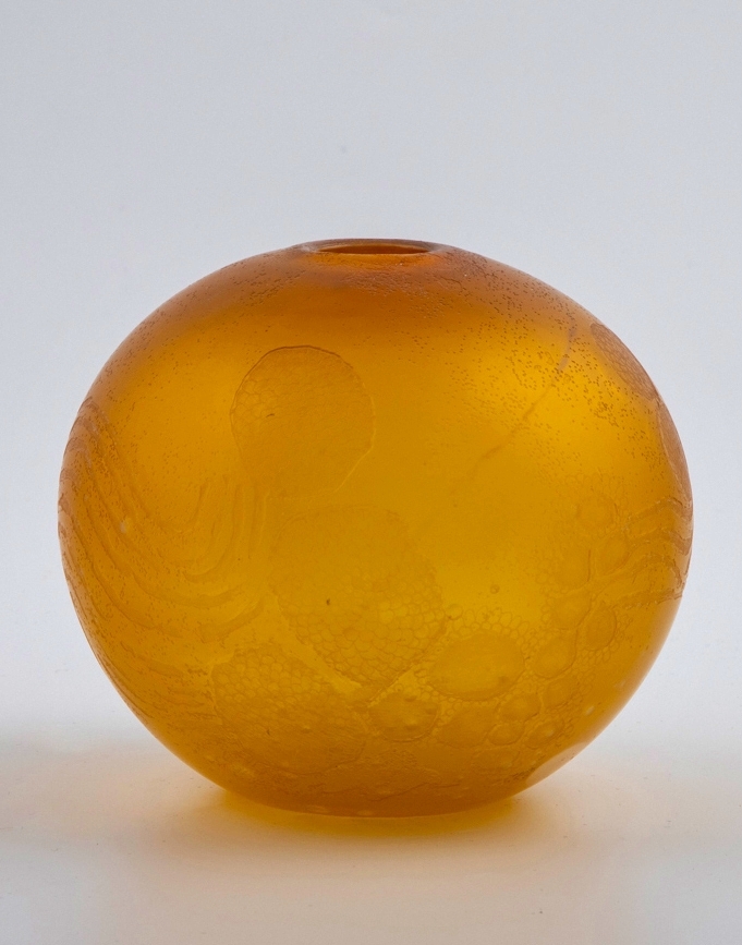 Kuleformet vase med liten rund åpning. Syrebehandlet gulbrunt glass med store og små luftbobler, samt hvitfarget parti på den ene siden.