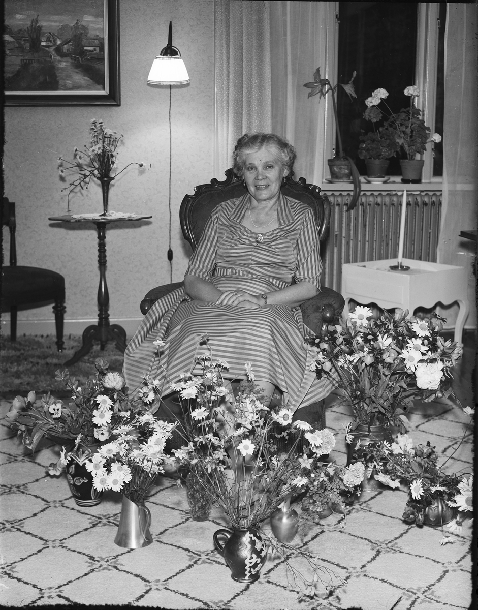 Kvinna i hemmiljö omgiven av blommor, Östhammar, Uppland
