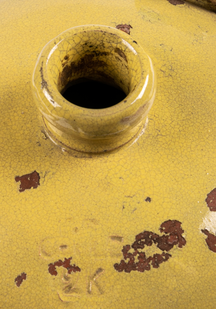 Brännvinskrus, gulglaserat lergods, drejat med en hänkel. Tillverkat vid Bo Fajans, stämplat på undersidan B GEFLE 2 K.