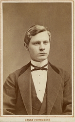 Foto av en ung man i kavajkostym med sammetskrage, väst, stä