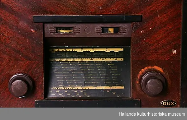 Radioapparat av märket Dux Typ U75. Uttag för grammofon. Lik- och växel-ström. Fronthögtalare, tygklädd högtalaröppning. Mångkantiga knappar.Rikliga stationsmarkeringar.Bredd: 40 cm.Djup: 31cm.Höjd: 44 cm. 