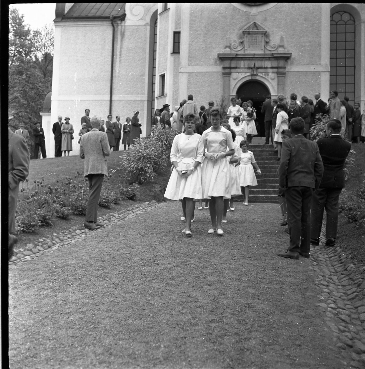 Kvinnliga konfirmander på väg ut ur Gränna kyrka. Deras väg kantas av barn och vuxna.