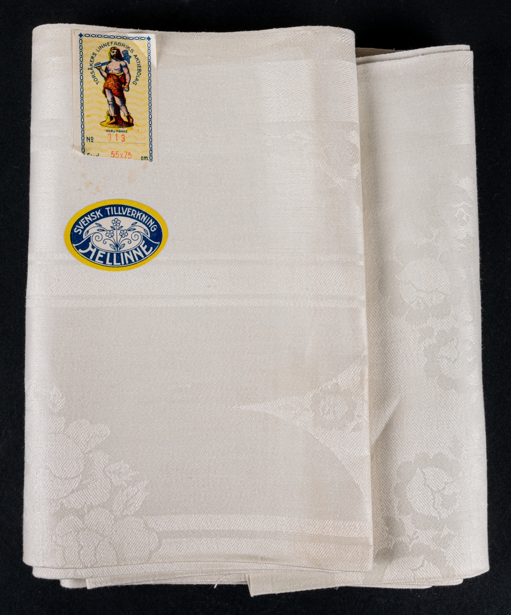 Oklippt, maskinvävd bordduksväv av hellinne, vit med vävda mönster, damast. Tillverkad vid Torsåkers linnefabriks aktiebolag.
Försedd med pappersetiketter med tillverkarens emblem