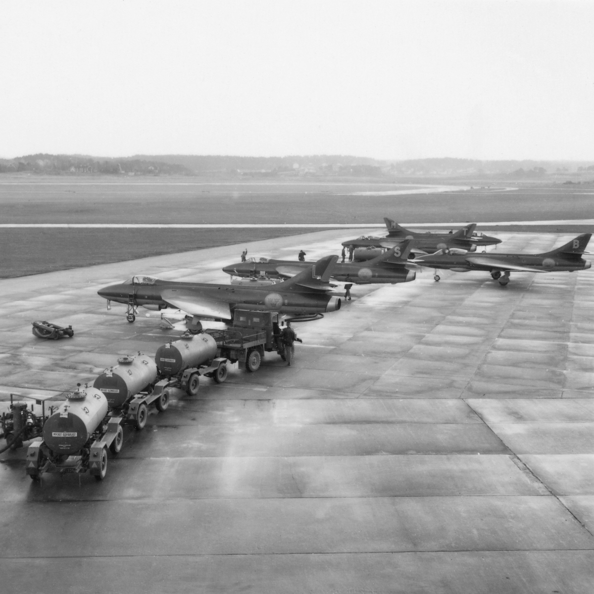 Klargöring av fem stycken flygplan J 34 Hawker Hunter på F 8 Barkarby flygfält. Bränsletunnor på vagn framdragna med jeep.