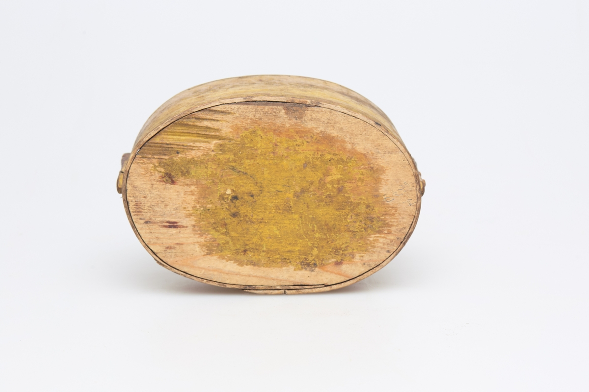 Oval tine (b) med lokk(a), gulmalt, laget av tjukk og bred høvelspon. To oppstandere holder lokket fast. Sviornamenter, tverrsittende håndtak på lokket, der det er påmalt K F D 1872.