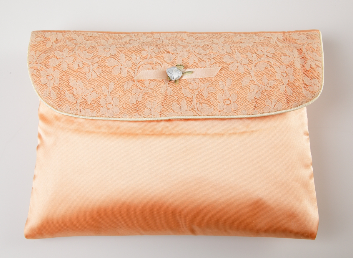 Aprikosfärgad väska i duchesse. Lock klätt med spets i blommigt mönster. En passpoal löper i sömmen på locket. På locket är en ljusblå blomma fastsatt på ett 60 mm aprikosfärgat band. 

Inskrivet i huvudkatalogen 1997.