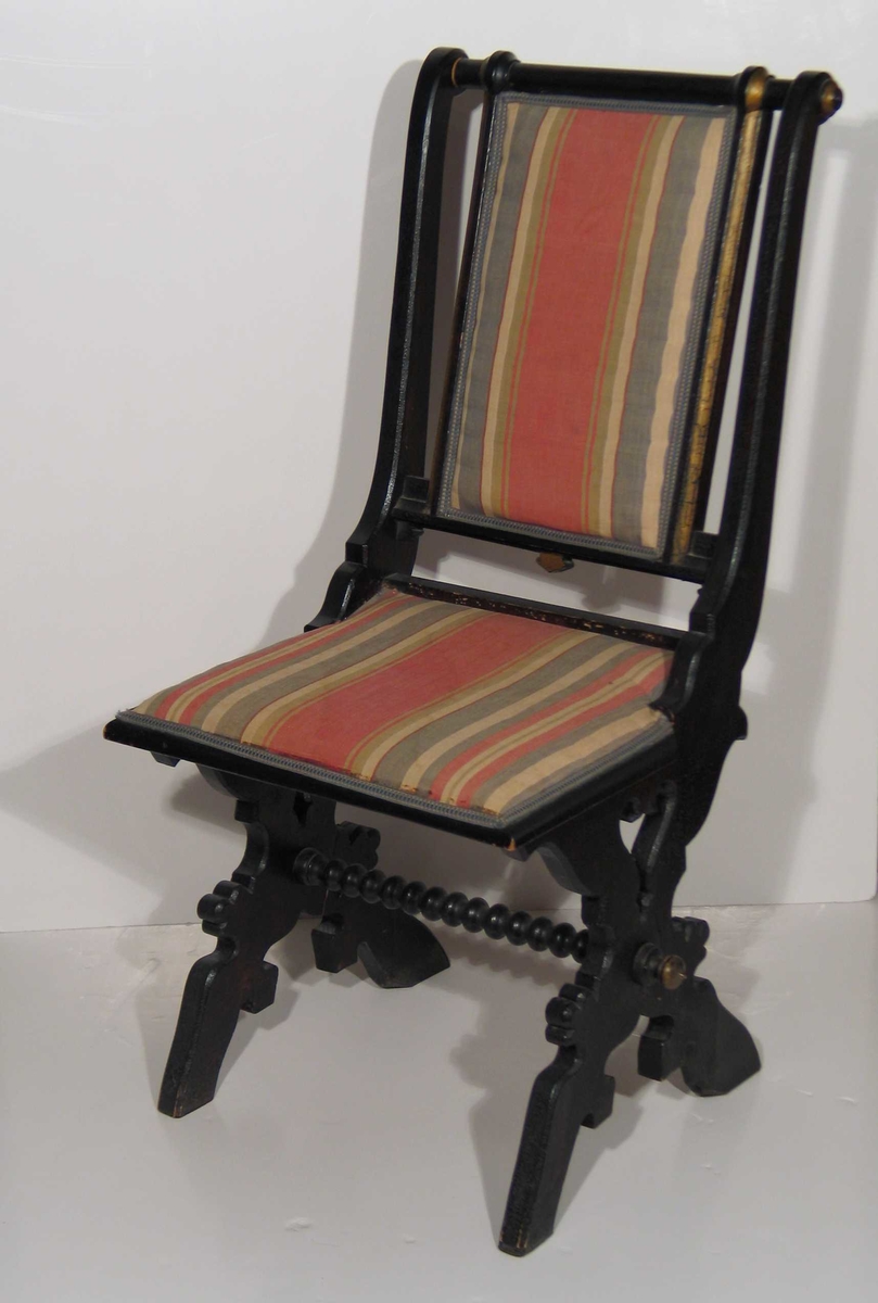 Svartmalt stol med kraftige profilerte bukkeben og kuledreid sprosse mellom. Rygg og sete trukket i et flerfarget stripet stoff. Gullmalte detaljer på rygg og sprosse.