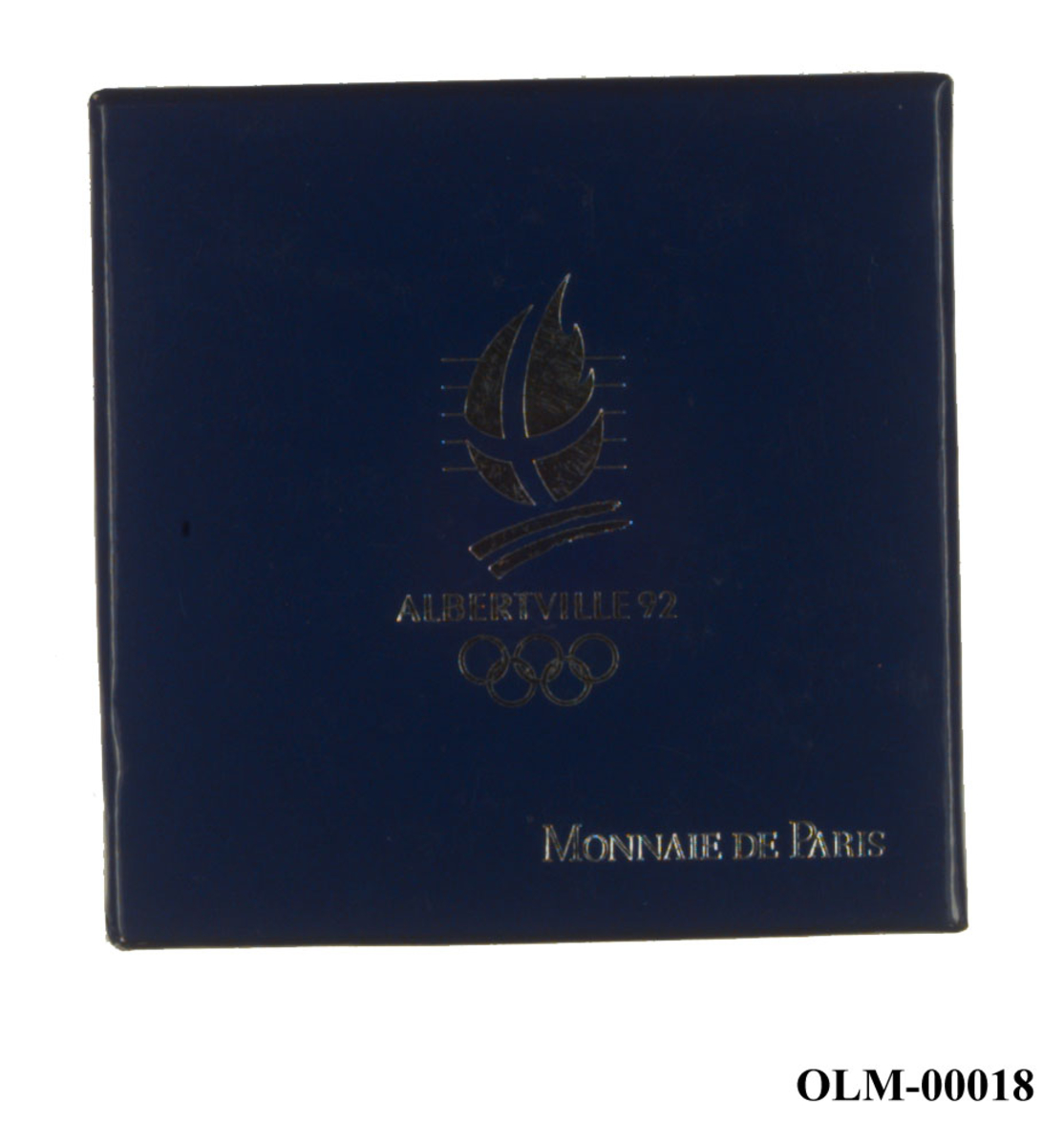 Sølvfarget minnemedalje med emblemet for de olympiske vinterleker i Albertville i 1992 og motiv av en stjerne over alpene og de olympiske ringene. 