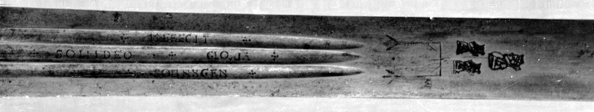 Skarprettersverd.  Pæreformet knapp med fasettetert dekor.
Tregrep viklet med rokkeskinn. 
Rette åttekantede parérstenger som ender i to dråper med kantet dekor. Rett tveegget klinge med ovalt tverrsnitt  og tre korte blodrender på hver side. Innslått tre smedstempler med kronede hoder.  På den ene siden er det gravert inn et hjul og på den andre siden en galge. Begge inngraveringer er innlagt med kobber.

