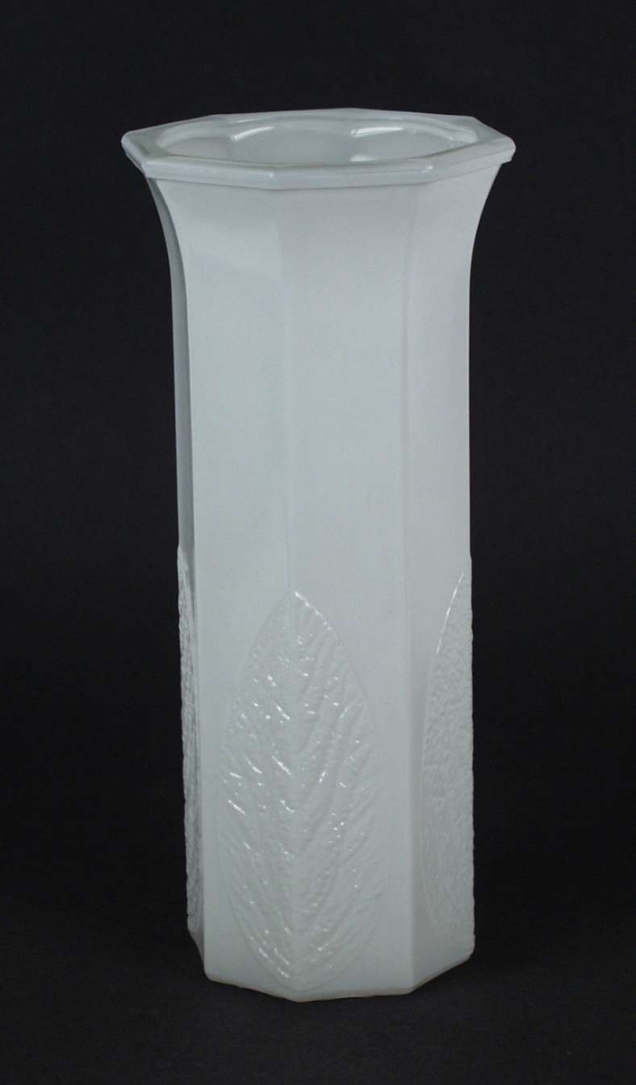 Hvit åttekantet vase i glass med bladmønster nederst.