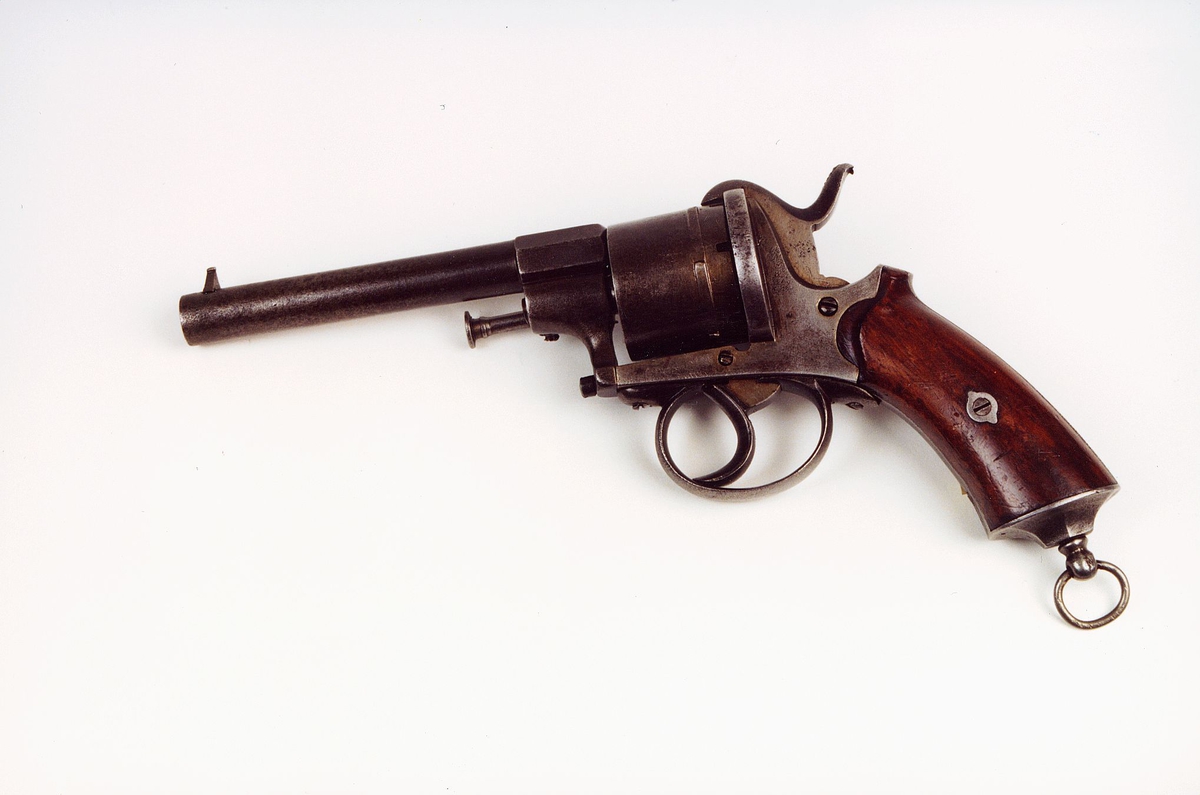 Selvspennende revolver av system Lefaucheaux, ca 1880, sylindrisk løp. Treskjefte. På trommelen belgisk kontrollmerke, ELQ, som viser at revolveren er prøveskutt og godkjent av myndighetene for bruk med sortkrutt. Kaliber 9 mm,  Prod. ca. 1880