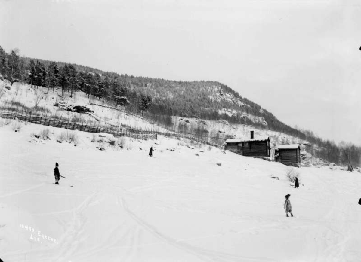 01.01.1908. Vinterparti med Byhrhagen. Gårdsbygninger, trekledd åsside, to personer på ski, to personer til fots, skispor, vinterbilde.