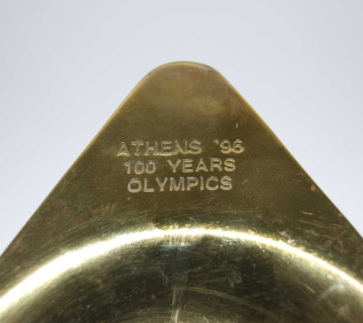 Gullfarget fat med en type medalje festet i bunn. Medaljen har samme motiv som minnemedaljen fra de olympiske leker i Athen i 1896. På medaljen er det motiv av seiersgudinnen Nike med Akropolis i bakgrunnen.