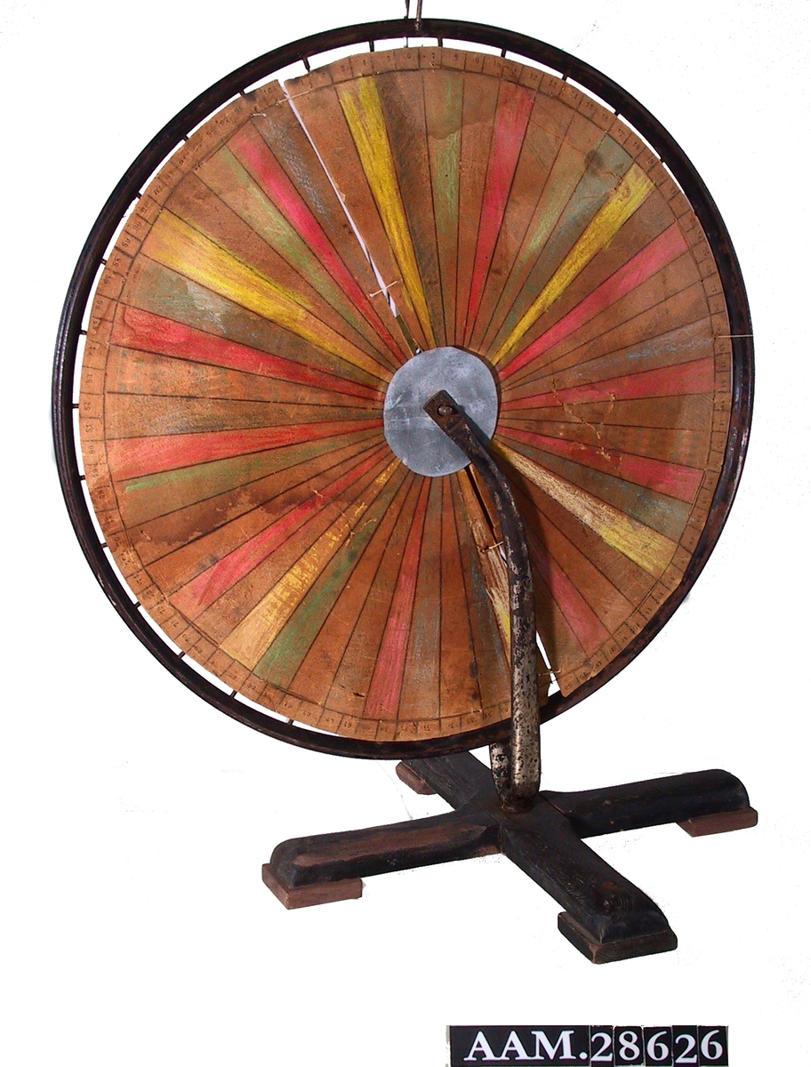 Laget av et sykkelhjul med påmontert en sirkelrund pappskive; hjulet står i en sykkelgaffel montert på en fot som likner en juletrefot. Pappskive i sektorer i ulike farger. Pappskiven er bundet til sykkeleikene med tråd. 