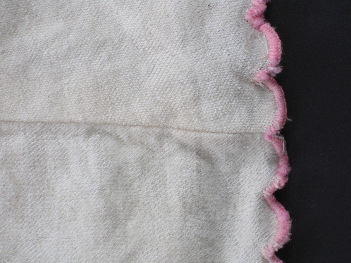 Form: Sammensydd av utskrådde høyder, linning, 2 folder på hver side av åpning midt bak. Lukkes med to hekter i linning. Nedrekant klipt i bølger, sårkant oversydd med rosa ulltråd.
