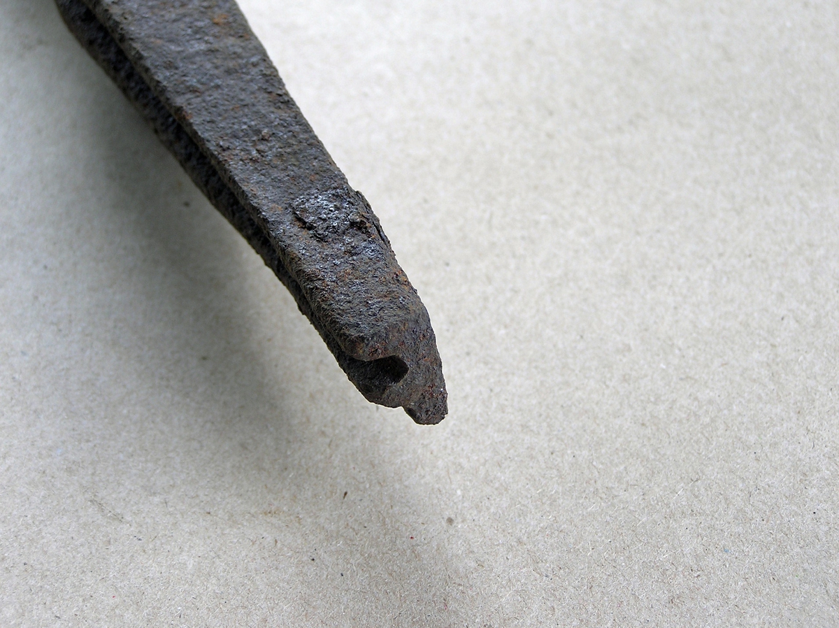 Smidd jernstykke til bruk ved smiing av merkeøks. Merket ble formet rundt stempelet. Stempeldel og håndtak i ett. F-formet stempel. En del rust.
