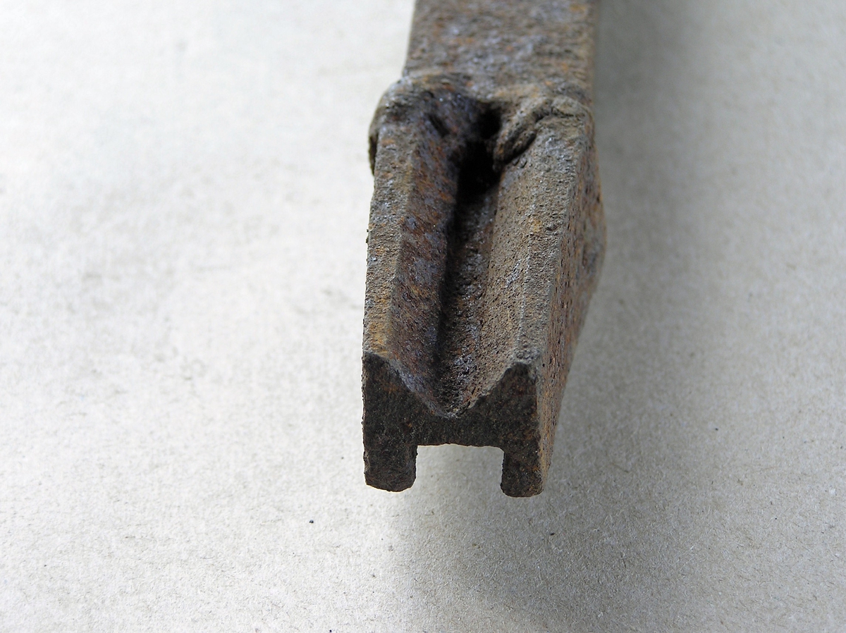 Smidd jernstykke til bruk ved smiing av merkeøks. Merket ble formet rundt stempelet. Svært tydelige sveiseskjøt mellom stempeldel og håndtak. M-formet stempel. Noe rust.