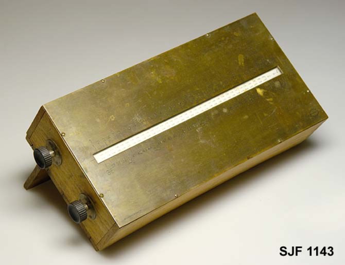 Kubikkberegningsapparat, levert av produsenten F. A. Krog i Skovveien i Kristiania, antakelig tidlig på 1900-tallet.  Apparatet er formet som et rektangulært skrin, utført i eiketre, men med "lokk" av ei messingplate.  Langs midtaksen på dette lokket er det ei lang, smal, rektanuglær spalte med glass under.  Gjennom denne ser vi ned på en tabell.  Tabellen er trykket på en papirrull, som er forankret på to valser nede i skrinet.  Tabellen kan beveges ved hjelp av dreiehjul på skrinets endeflater, to på hver side, ett i hver ende av de nevnte valsene. Ett av hjulene mangler på dette eksemplaret. Lengst til høyre i tabellvinduet finner vi "klassifiseringsinformasjon" - angivelser av stokklengder, diametere og salgsklasser.  Langs den øvrige delen av vinduet kan man lese av kubikkmeterangivelser for fra 1 til 70 stokker med samme dimensjoner og klassespesifikasjon.  Avlesinga skjer fra en tolinjet tabell på den nevnte papirrullen inne i skrinet, og med stokketallesangivelser på lokket - 1-35 stokker på oversida av vinduet og 36-70 stokker på undersida.  Det nevnte emaljerte lokket, som er hvitt med svarte tall og bokstaver, er skrudd fast til toppen av skrinet.  Det er grunn til å tro at valsene med tabellen må være montert før dette ble påsatt.  Skrinet er ellers lagd av høvlet eiketre, og den holdes sammen av de nevnte skruene i lokket og spiker fra botnstykket.  På standflata er det også hengslet en klaff, som kan vippes opp, slik at lokket skrår mot brukeren når apparatet brukes på et bord eller et annet plant underlag.
