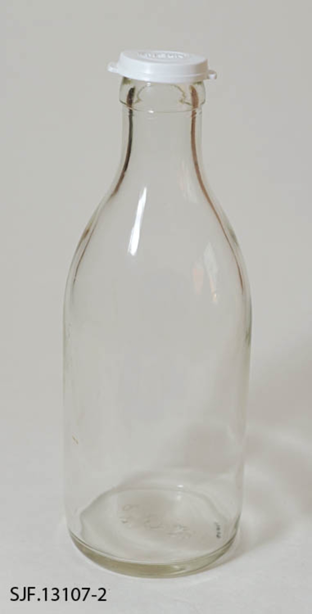 Melkeflaske bestående av flaske og lokk. Flaska er lagd av klart glass. Den er er 25,6 centimeter og har en sylindrisk kropp med 9,5 centimeters diameter. Cirka 14 centimeter ovenfor standflata skrår flaska slakt innover mot en krage rundt munningen. Her er diameteren (utvendig) 4,0 centimeter. I bunnen av flaska er det en del symboler i opphøyet relieff, blant annet noe som ser ut som en sammensmeltning av bokstavene «M» og «G» (som indikerer at dette er et produkt fra Moss Glassverk) samt «P4» og «63». Flaska kan romme et væskevolum på 1 liter. Melk ble levert i slike flasker, med en foliekapsel over flaskemunningen. For å kunne lagre rester etter at foliekapselen var brutt hadde husholdningene gjerne en del plastdeksler som kunne gjenbrukes hver gang ei flaske med melkerester skulle settes til side i påvente av at resten av innholdet skulle konsumeres.  Denne flaska ble avlevert til museet med et kvitt plastdekksel med ordet «MELK» i opphøyet relieff på oversida. Dekselet er sirkelrundt, men har to utstikkende «ører» eller «flipper», plassert diameteralt overfor hverandre, som ble brukt når dekselet skulle løsnes.