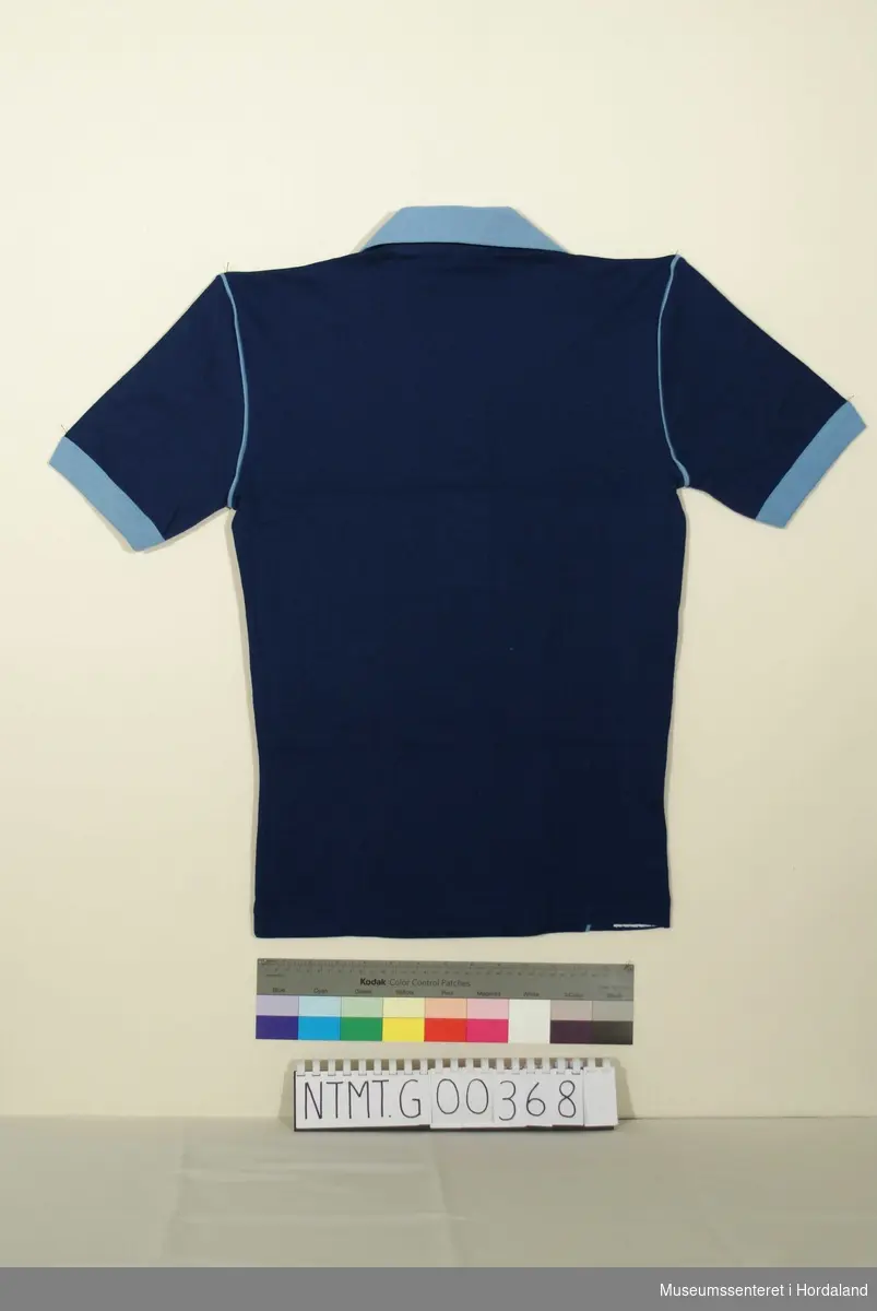 Mørk blå t-skjorte med lys blå krave, knappeåpning i hals med to knapper, lys blå knappestolpe, lys blå kantavslutning ermer.