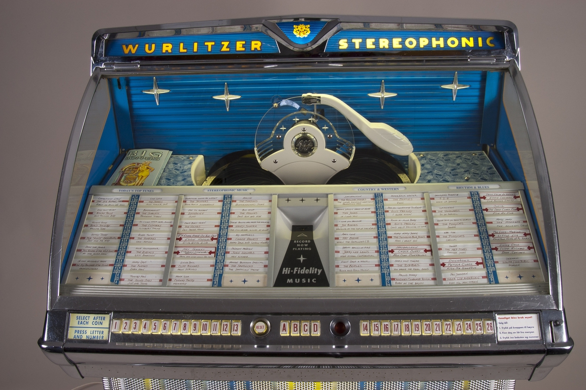 Jukeboks i krom, med stereolyd. Kan velge mellom 104 låter fra 52 vinylsingler ved å trykke på knapper på fronten. Myntinnkast.