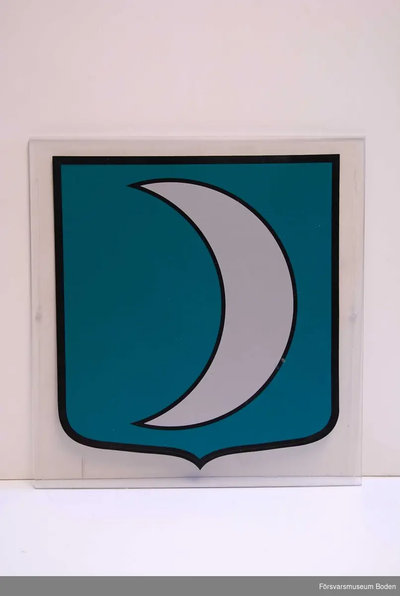 Dekal på plexiglasskiva med ett hål på vardera sidan för uppsättning. Okänd symbol i form av en halvmåne.