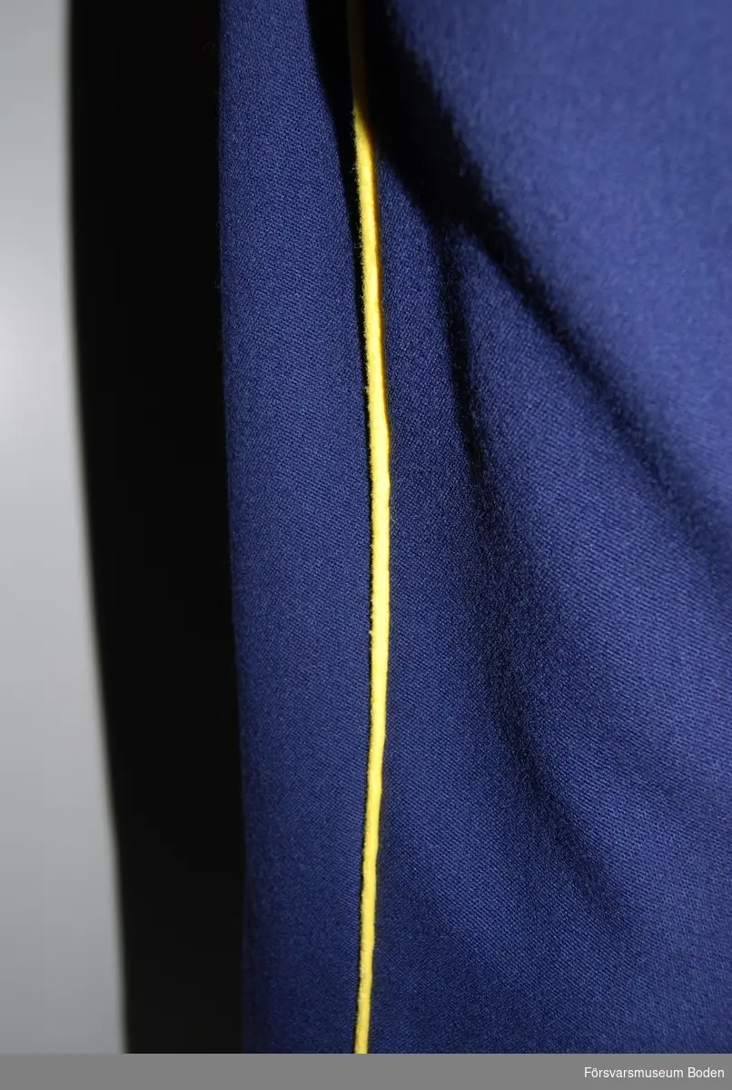 Mörkblått kläde med gula passpoaler längs yttersömmarna. Knappar på byxbenens insida nertill vid anklarna.