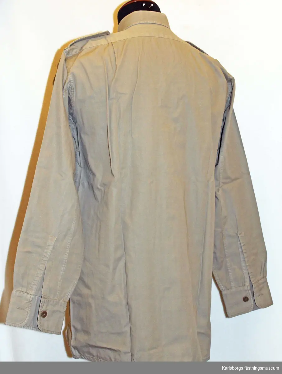Skjorta m/1952 avsedd för tropikdräkt. Långärmad, med nedvikt krage, påstickade bröstfickor med knäppara ficklock. Har använts vid FN tjänstgöring. Storlek 39.