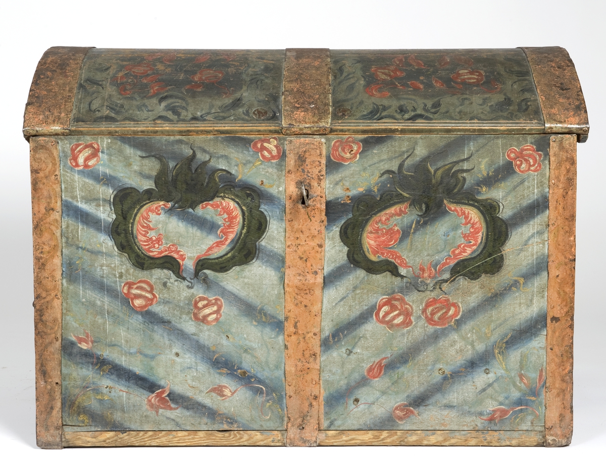 Kiste med buet lokk og smijernsbeslag og bånd. Rosemalt lokk og tre sider. Innvendig rosemaling delvis vasket bort.