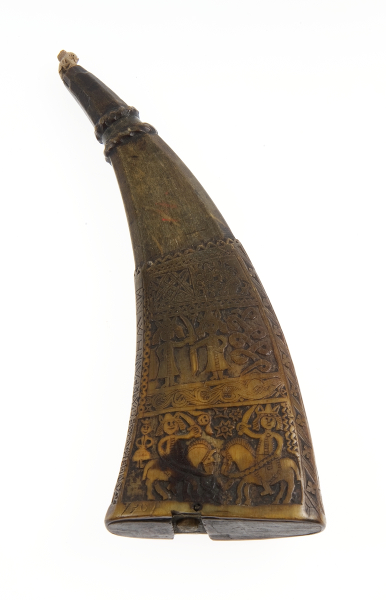 Krutthorn med flat bunnplate i tre. Skåret ornamentikk på horn i form av tre felter med mennesker og dyr og en mengde bårder med forskjellige ranker, figurer, geometriske mønster og tekst.