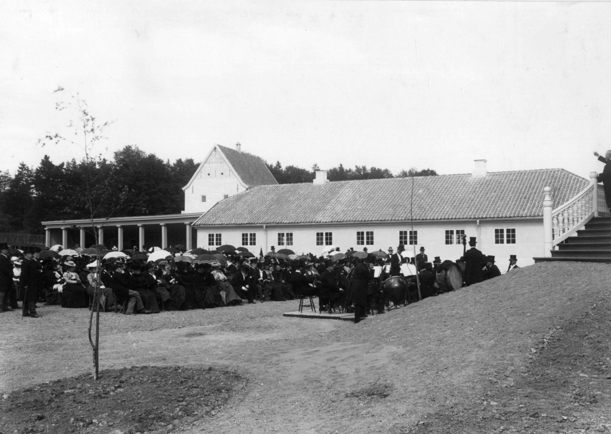 Direktør Hans Aall åpner Den kulturhistoriske utstillingen i 1901.
Publikum og musikkanter lytter til Aall, som står på trappen og taler.