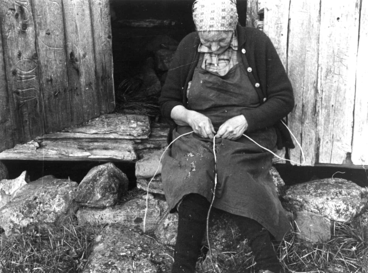 Frøysnes,  Bygland, Setesdal, Aust-Agder 1941. Fru Gyro sitter på en stein utenfor et hus og kløyver teger.