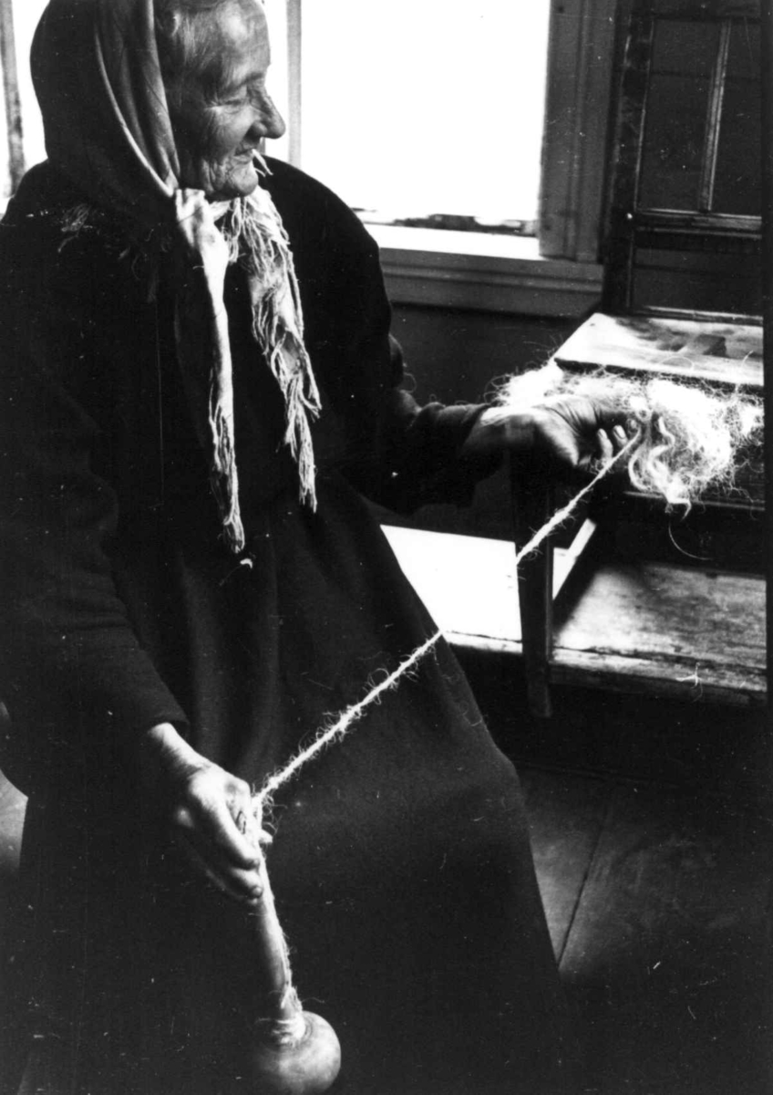 Ragnhild Åvitsland spinner kutagl og grov ull på en liten hjemmelaget håndrokk i tre. Eiken, Hægebostad, Vest-Agder 1941.