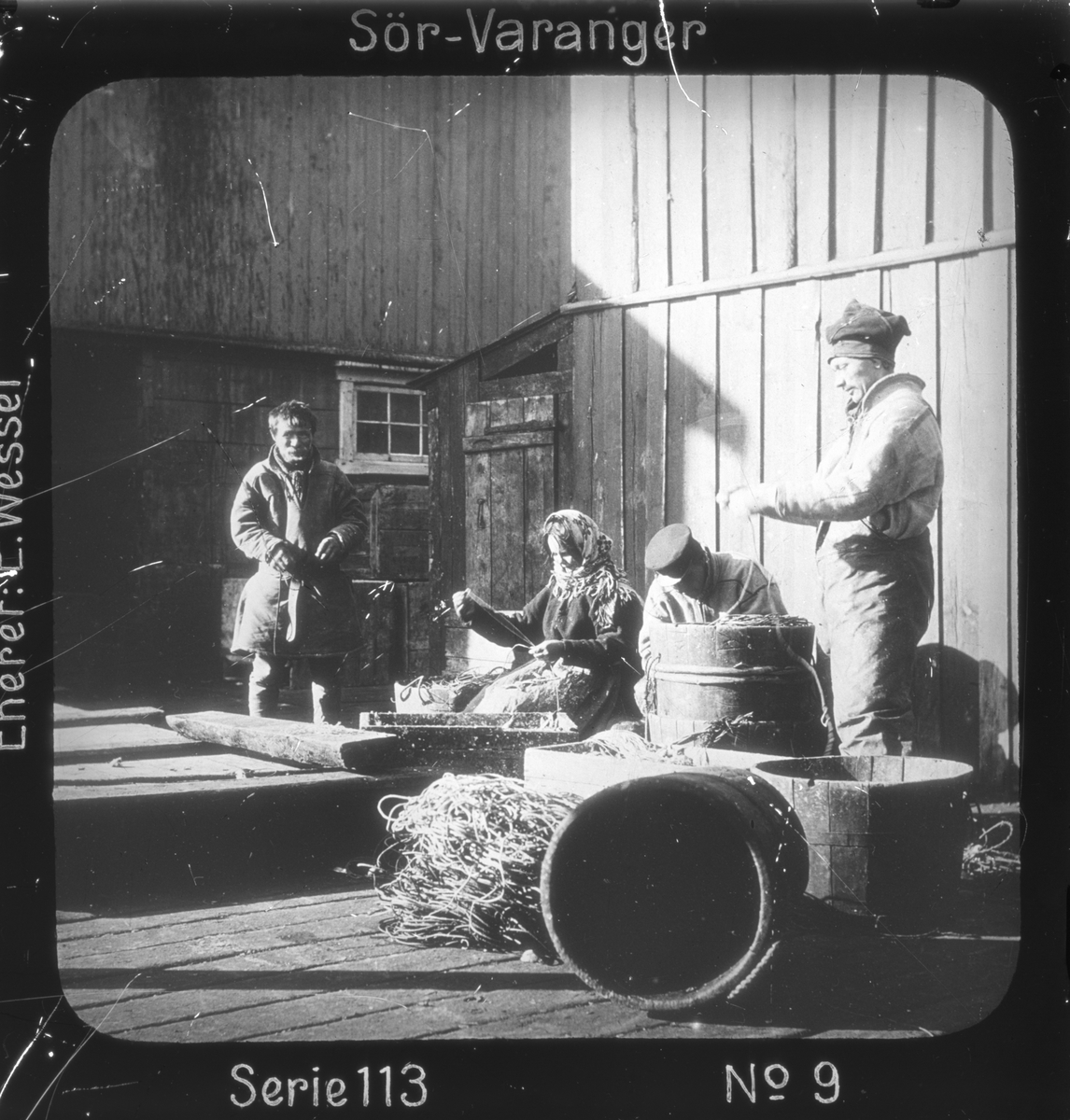 Samiske fiskere setter agn på liner i fiskeværet Kiberg, Vardø, Finnmark. Linestamper i forgrunnen. 
Motivet har nr. i lysbildeforedraget kalt  "I lappernes land - Sør-Varanger", utgitt i Nerliens Lysbilledserier, serie nr 113. 