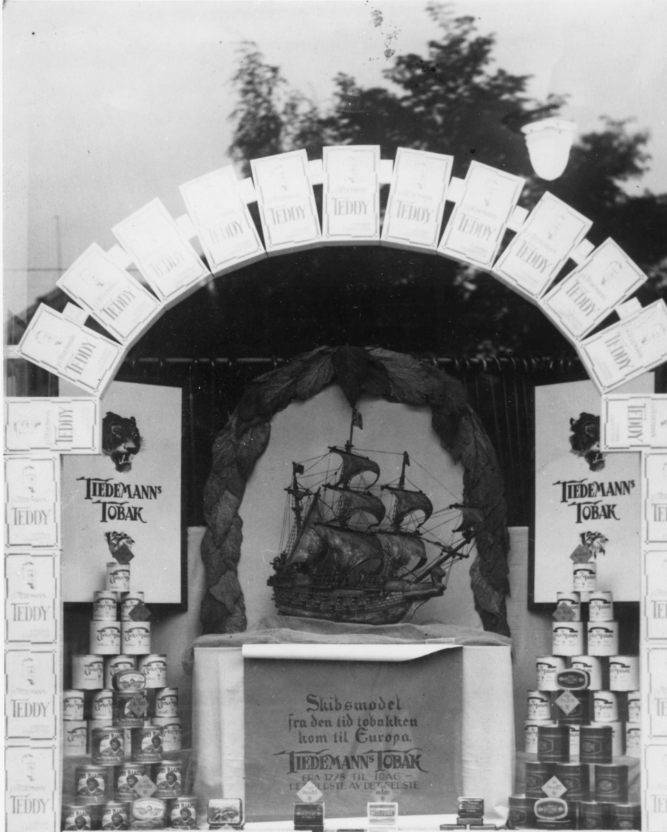 Vindusutstilling med reklame for blant annet Tiedemanns Teddy sigaretter. Også utstillt en modell av et skip som skal vise hvordan skipene som kom til Europa med den første tobakken så ut.