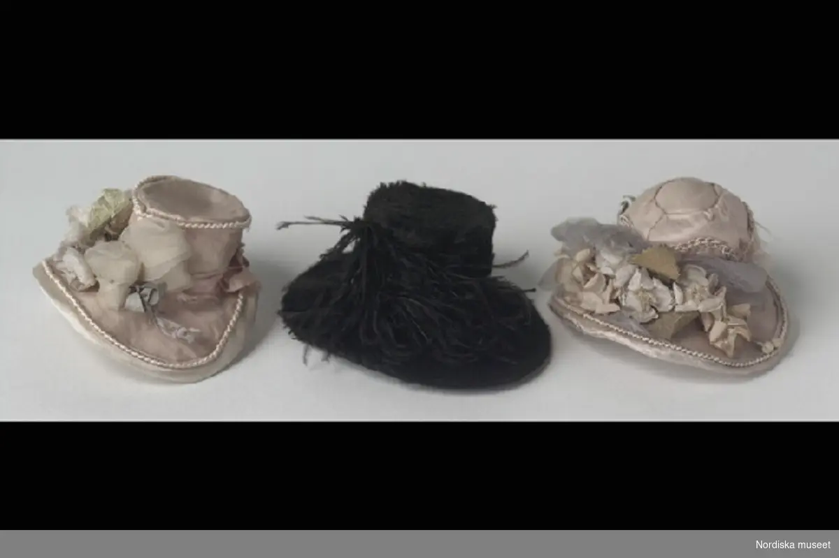 Inventering Sesam 1996-1999:
H 31 (cm) 
Docka, damdocka, 2 st, "Fru och Mamsell Medberg", huvud med sköld av papier maché, krederat och målat, och kropp i stoppat tyg, b) med skinnarmar. Målade ansiktsdrag, röd sluten mun, svarta ögon och enkelt svartmålat hår med tinningslockar. Strumpor av vit bomullstrikå och svarta, platta sidenskor fastsydda på kroppen. a) med halsband av glaspärlor.
Lintyg, 7 st (c-i), av vitt linnetyg, med kort ärm, några spetsprydda, (g) och (i) med broderat "j". Kalsonger, 7 st (j-p), av vitt bomulls/linnetyg, (j) och (o) med brodyr nedtill. Underkjolar, 6 st (q-v), av vitt linnetyg. Nattröja, (x), av vitt linnetyg, lång puffärm, krage med spetskant och knytband i halsen. Kjolar, 3 st, z) av grönt siden med färgade bårder nedtill, saknar linning, y) av svart siden, saknar linning, å) av grönt linnetyg, med 2 st rosa bårder, paljetter och fåll med insydd snodd. Klänningar, 2 st (ä,ö) av randigt sidentyg i rosa och vitt, med kort ärmpuff, tvärgarneringar och insydda snoddar. Klänningar, 10 st, med lång ärm, a:1) svart siden, 
tvärgarneringar nedtill, b:1) gräddvitt siden, kort ärm, c:1-d:1) 2 st, vitt bomullstyg med ljusbruna prickar, e:1) bomullstyg, tryckt, vitt med blå blad- och blommönster, kjolen med volanger nedtill, f:1) bomullstyg, randat i vitt, ljusblått och mörkblått, g:1) bomullstyg, tryckt, vitt med rött vegetativt mönster, gigotärm, h:1) bomullstyg, randat i rött och vitt, 2 st snoddar insydda nedtill, i:1) bomullstyg, vit- och rödrutigt, vita ärmar, "vingar" på axlarna, skärp av vitt sidenband och j:1) linnetyg, vit, kortärmad. Förkläden, 4 st, av bomullstyg, tryckt mönster, knytband, k:1) vit- och brunmönstrat, l:1) blå- och vitrutigt, m:1) vit- och rosamönstrat och n:1) röd- och vitrandigt. Slängkappor, 2 st, o:1), med kapuschong, violett ylletyg, fodrat med rosa siden och rosa kantgarnering och p:1) cape/slängkappa, av grönt ylle, fodrad med gult siden (på väg att fransa sig), med "vingar" och krage, dekorerad med grönt snörmakeri. Hattar, 4 st, q:1) bredbrättad, klädd med svart felb, dekorerad med svarta fjädrar, sidenfoder, vit tyll inuti, r:1) bahytt, klädd med rosa siden, prydd med tygblommor och silkessnoddar, knytband, vit tyll inuti, s:1) bahytt, klädd med ljusviolett siden, prydd med tygblommor och silkessnoddar, knytband, vit tyll inuti och t:1) bahytt, klädd med gräddvit siden, prydd med tygblommor, silkessnoddar och sidenrosett, knytband, vit tyll inuti.
Underkjol (v) saknas, januari 1997.                  
Anna Womack 1997