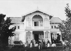 Familie i helgeklar i hagen foran rikt dekorert sveitserhus.