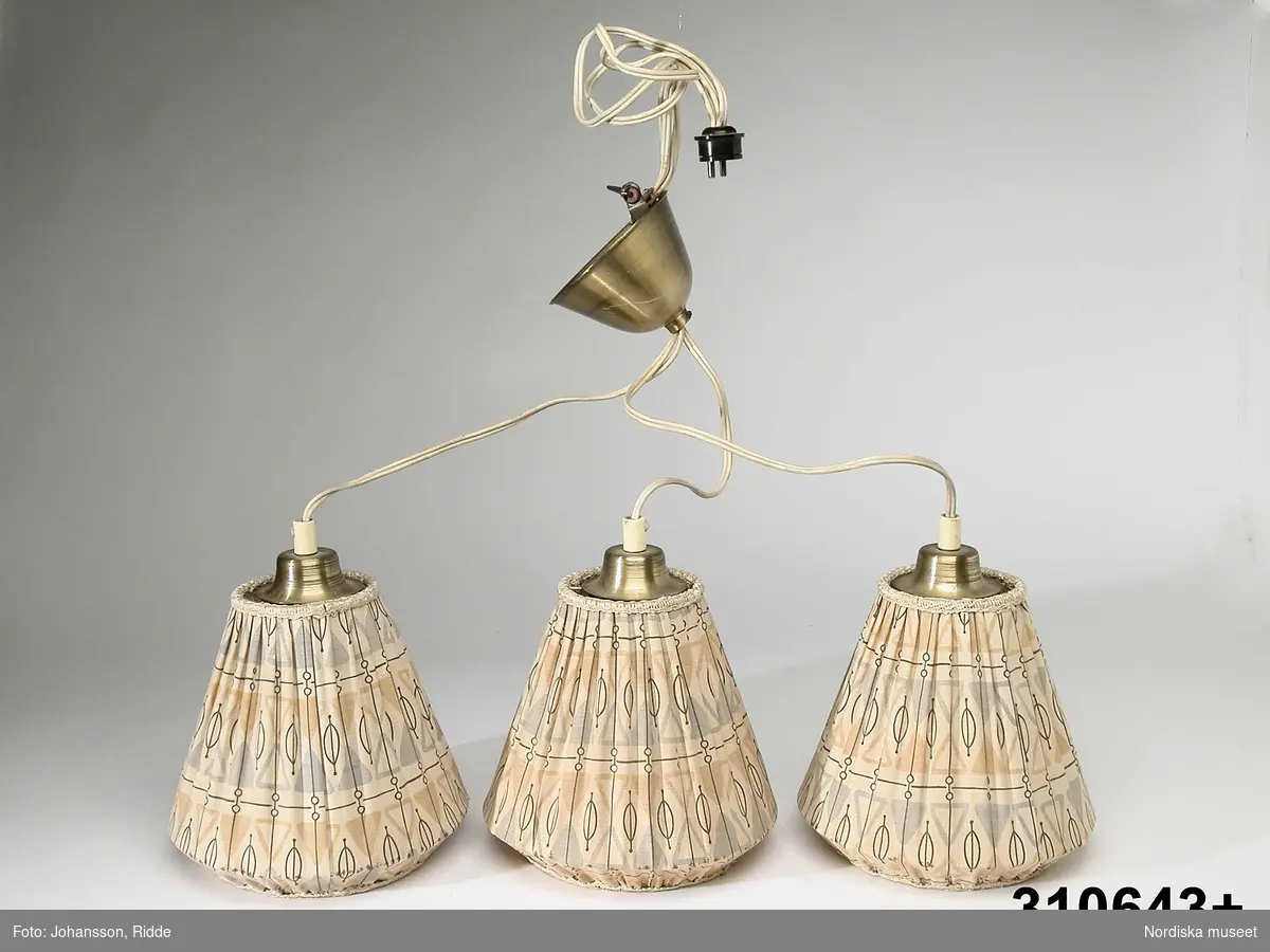 Huvudliggaren:
"Taklampa, elektrisk. Tre lampskärmar hängade i tre separata slddar på olika höjd, takhållare av mässing. Skärmar av veckat bomullstyug över konisk ståltrådsstomme, geometriskt tryckt mönster. Använd i givarens pojkrum ca 1955.