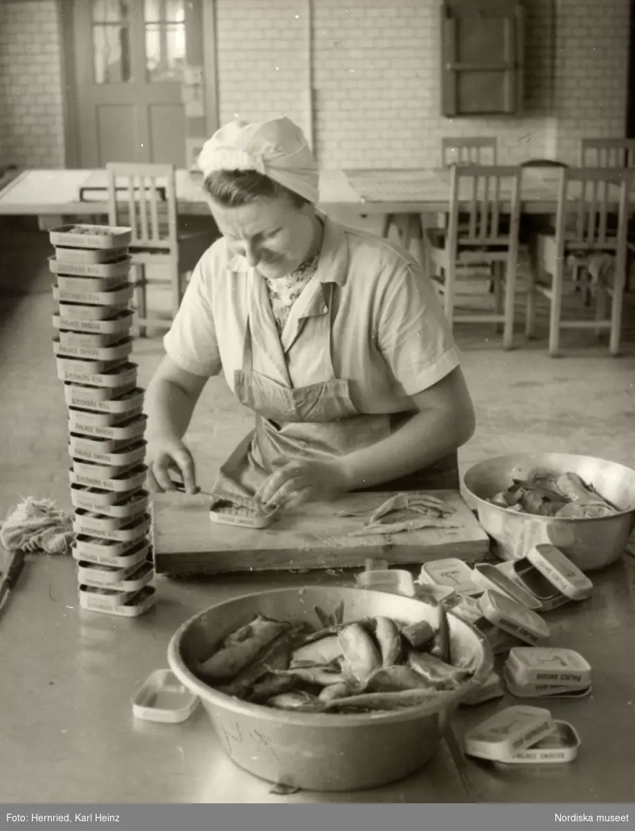 Sveriges Förenade Konservfabriker, AB i Lysekil, Bohuslän. Bolaget  grundades 1898 och förfogar över åtta fabriker. I Lysekil har man specialiserat sig på enbart sill- och ansjovisinläggningar samt kryddning och sockersaltning av skarpsill och sill. Produkterna går under namnet "Fyrtornet".
En kvinna sitter och rensar, skär sill i gaffelbitar som hon lägger i burkar med texten "Smörgås-sill" respektive "Palace snacks". 