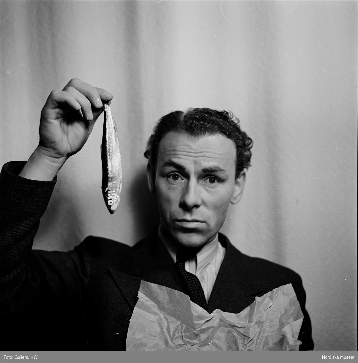 Nils Poppe (1908-2000), skådespelare och komiker, håller upp strömming med handen.