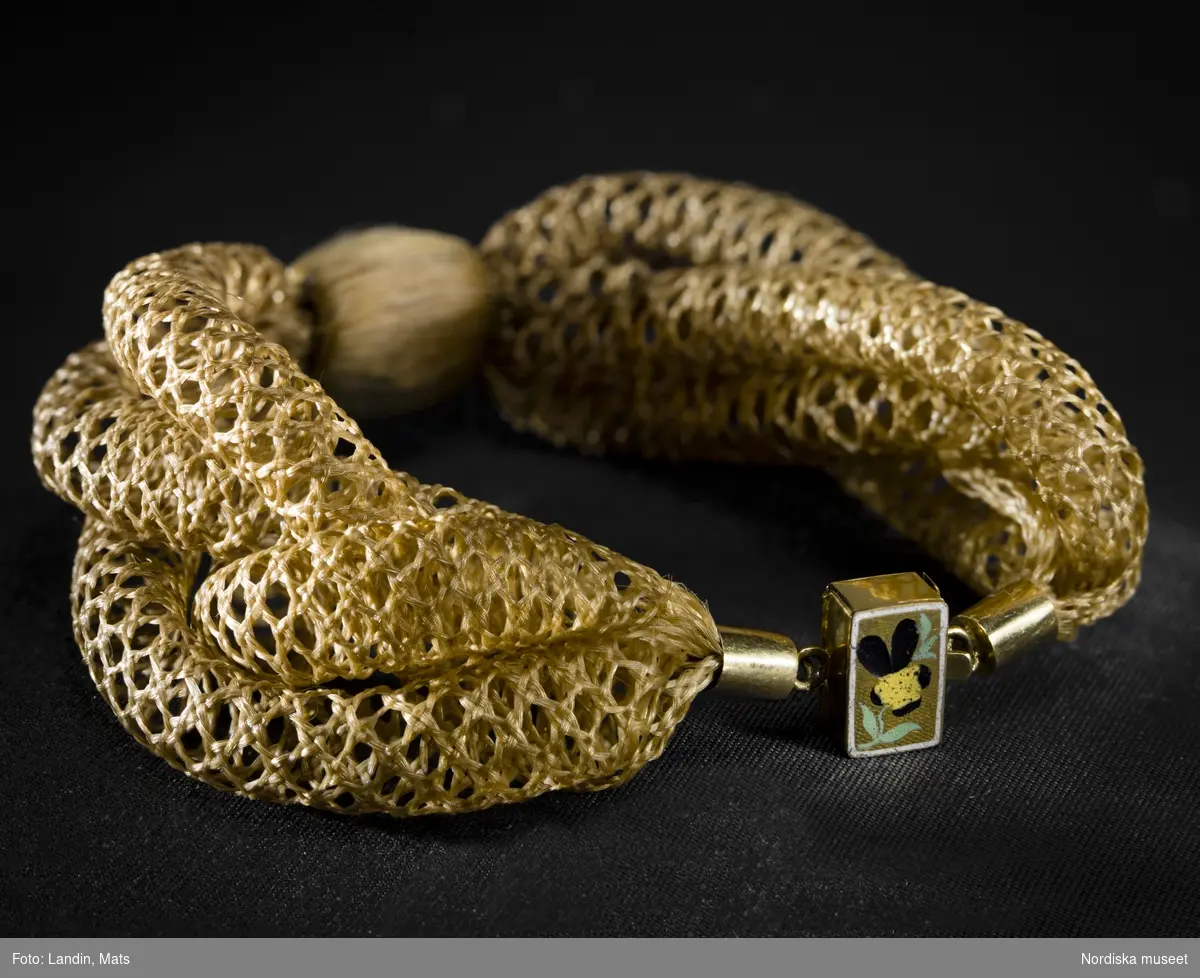 Smycke. Armband  tillverkat 1863 av hår från tre syskon födda 1856, 1858 och 1860. Spännet är i guld och emalj.
Föremål ur Nordiska museets samlingar :inv.NM.0314144+*1. Fotograferat för utställningen Smycken med öppningsdatum 2012-09-14.