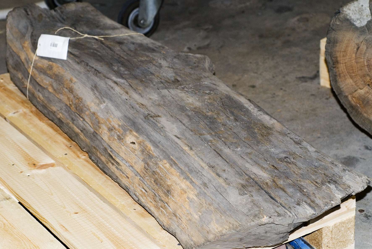 Stock av ek, kan eventuellt vara en del av brunnens väggvirke. På ena sidan en spik av järn.

Träet är mycket torrt och skört, skadas lätt vid hantering.

