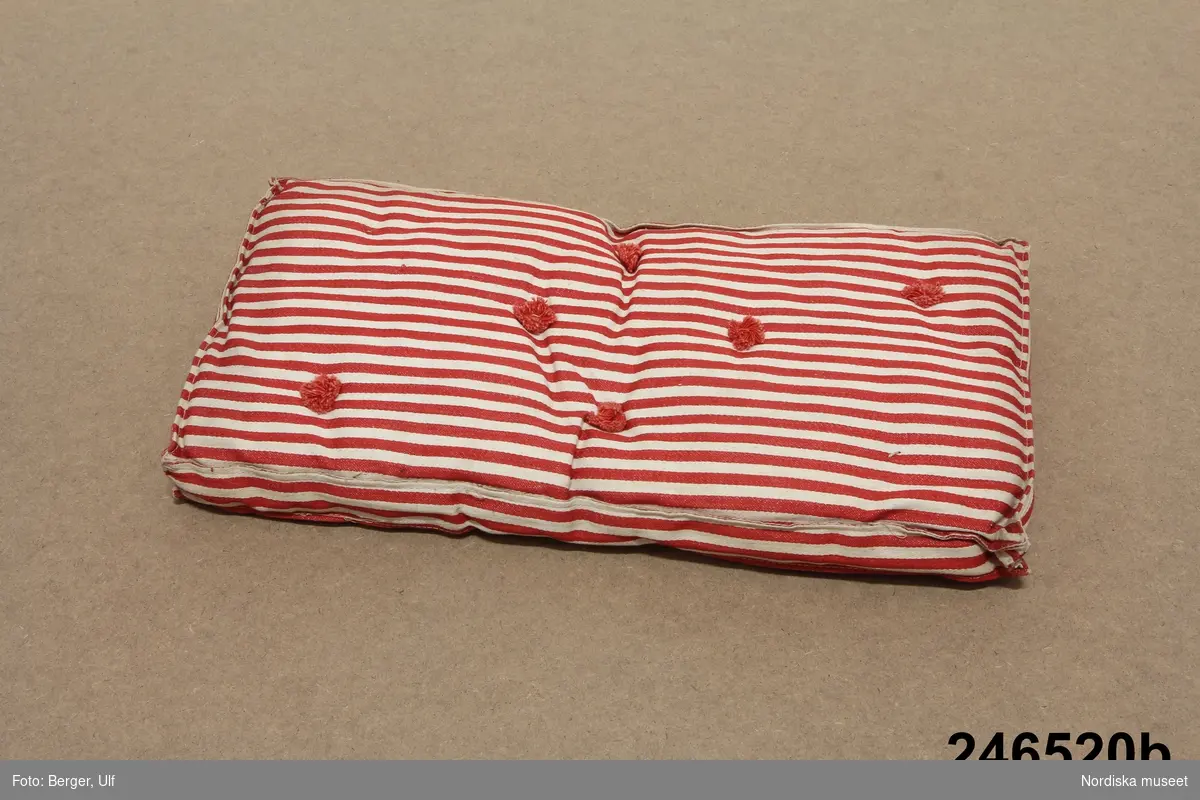 Inventering Sesam 1996-1999:
a) Järnsäng av enkel modell, av järnstänger i svart och guld, höga gavlar, botten av plåtband. L 41 cm, B 22 cm, H 39 cm
b) Madrass av röd- och vitrandig bomull, stoppad med tagel, röda puskor. L 40 cm
c) Bolster av röd- och vitrandig bomull, stoppada med fjäder. L 36 cm
d) Kudde (långkudde) av röd- och vitrandig bomull, stoppad med ull (el. liknande). L 20,5 cm
e) Kudde av röd- och vitrandig bomull, stoppad med ull (el. liknande). L 13,5 cm
Till sängen hör sängkläder inv.nr 246.521-246.527.
Leif Wallin april 1997
