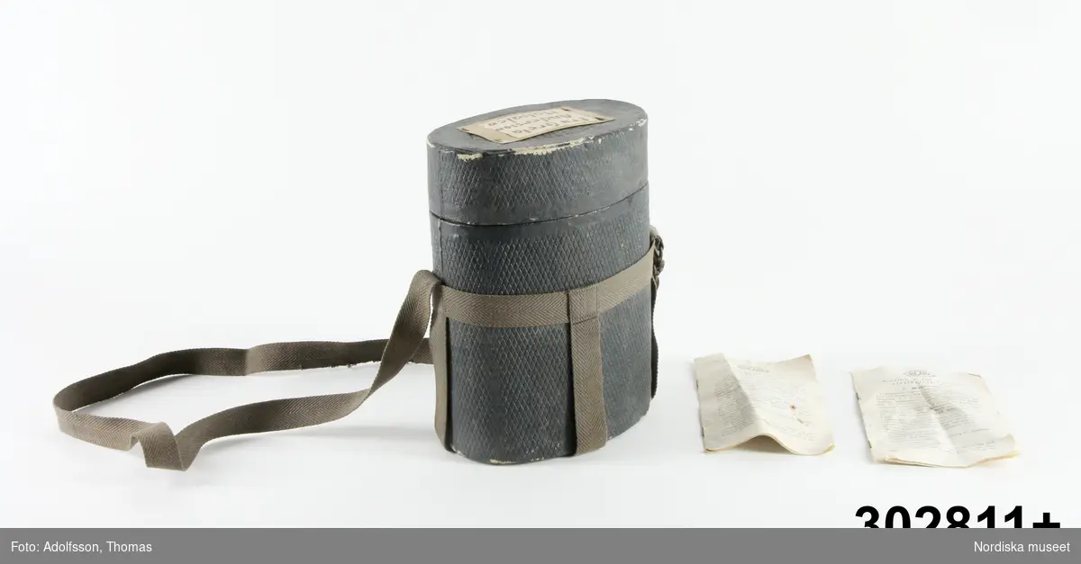 Huvudliggare:
"GASMASK med tillbehör; ansiktsskydd av tyg, ventilhus och behållare av vitmetall; grå förvaringsbox av kartong med axelrem; text 'För passivt luftskydd', tillverkad av Bicapa, Birger Carlsson & Co, Sthlm; tryckt bruksanvisning från 1939. (2 ex) St L ca 40 cm, box L 19 cm, br 12 cm, H 26 cm.
G Från Vin- & Spritbolagets fabrik på Reimersholme, Sthlm, avsedd f. anställda. 1978 18/7 Fröken Anette Rosengren, Stockholm."