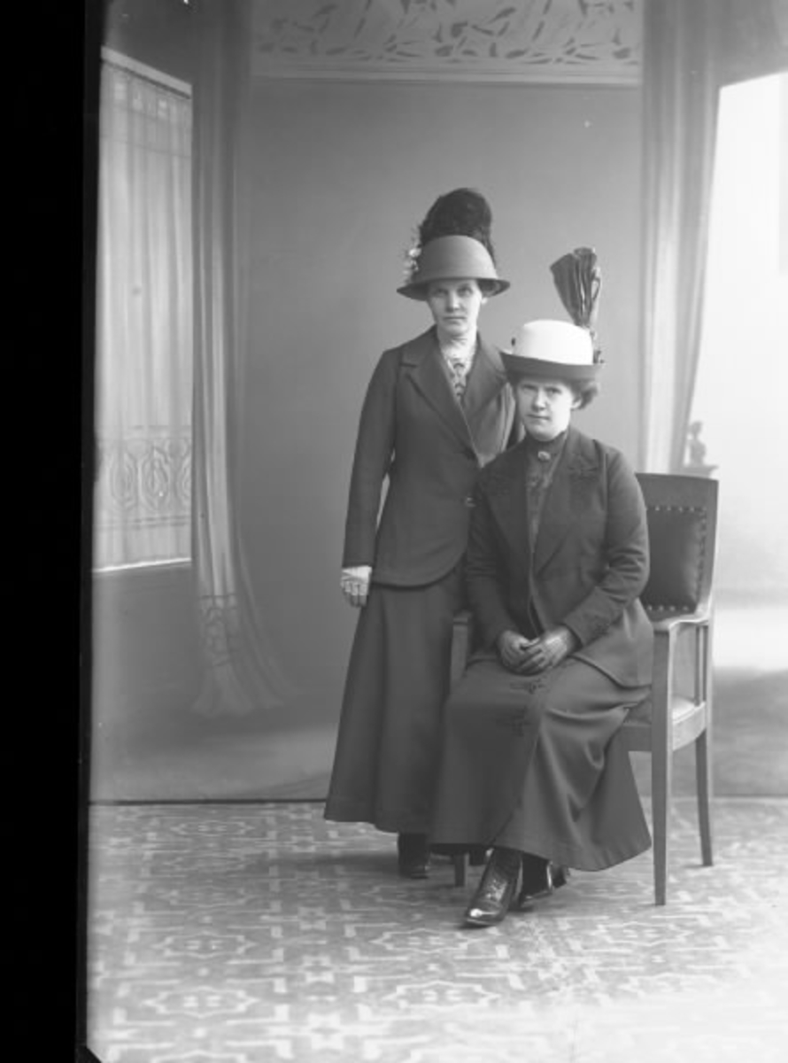 Porträtt av två kvinnor, båda klädda i hatt, ateljéfoto