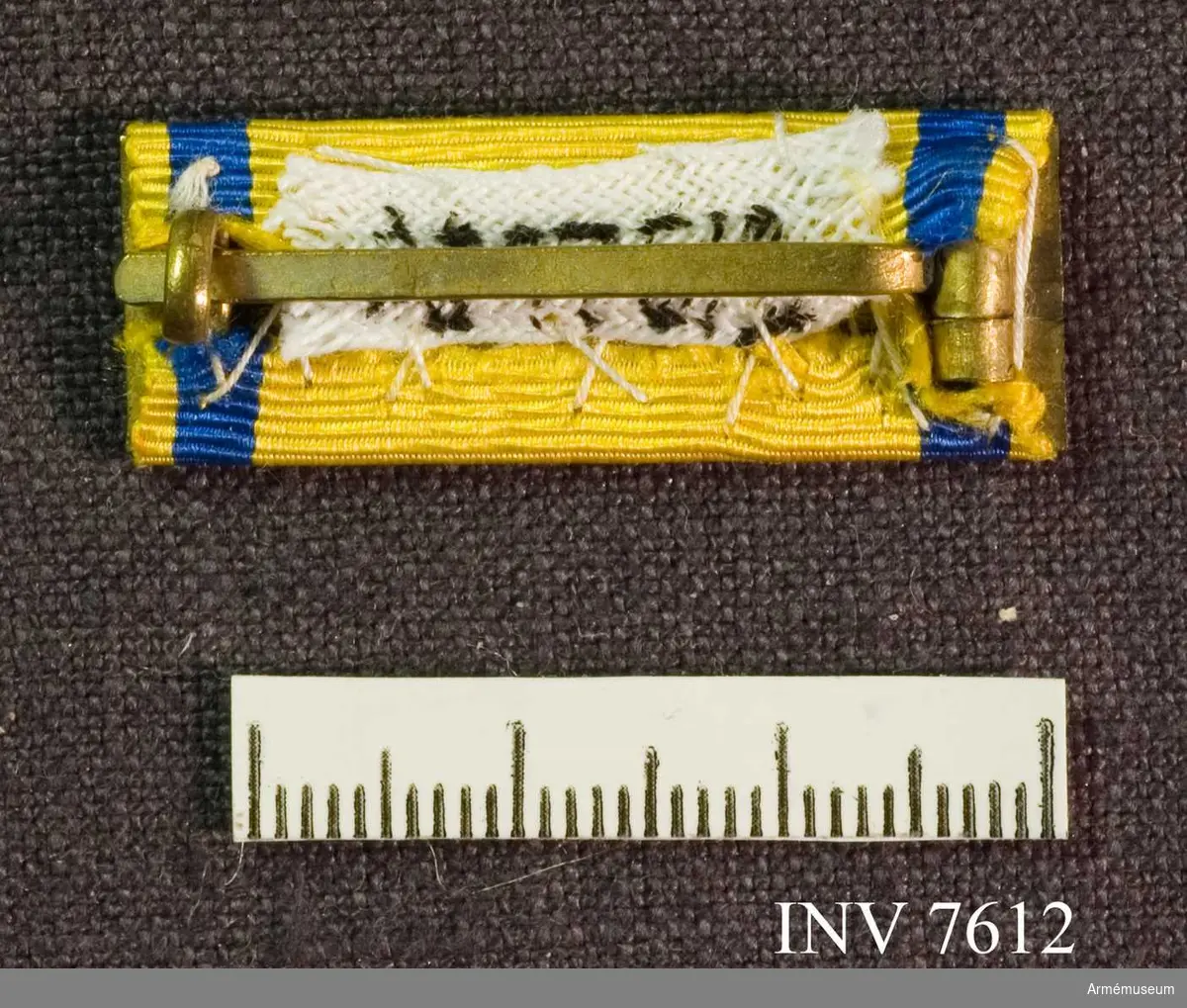 Metallspänne överklätt med samma band vad gäller färg och bredd som svärdstecknets band.

Förvaras tillsammans med AM 7611 i röd ask med gulddekor.