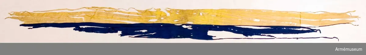 Duk av gult fyrskaftat fansiden. Fragment uppsydda på gult konstsiden. Fragmentet är från fanstången mot mitten 85 cm djupt. Stång 2.67 m lång av vitmålad furu. Doppsko saknas. Spets med Karl XV:s namnchiffer.