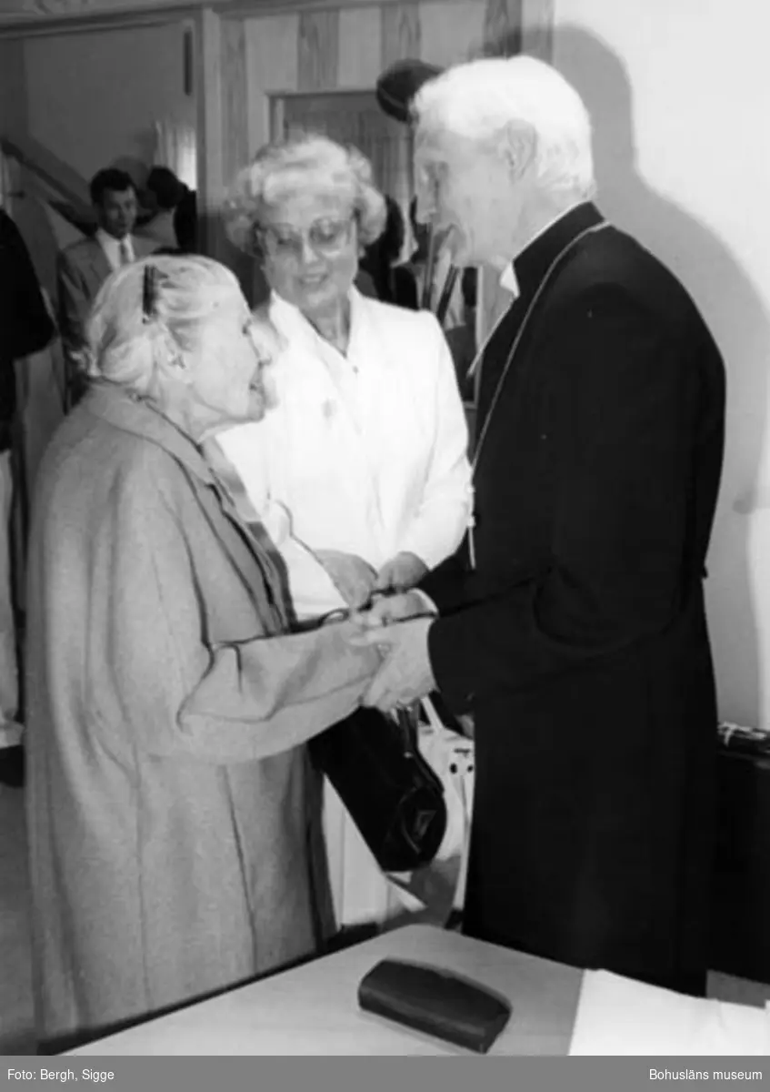 Enligt text på fotot: "Hunnebostrand Anna Andersson 100 år hälsar på Biskop Gärtner 1987. Anna dog 103 år gammal 1990 Fru Glädt i bakgrunden".