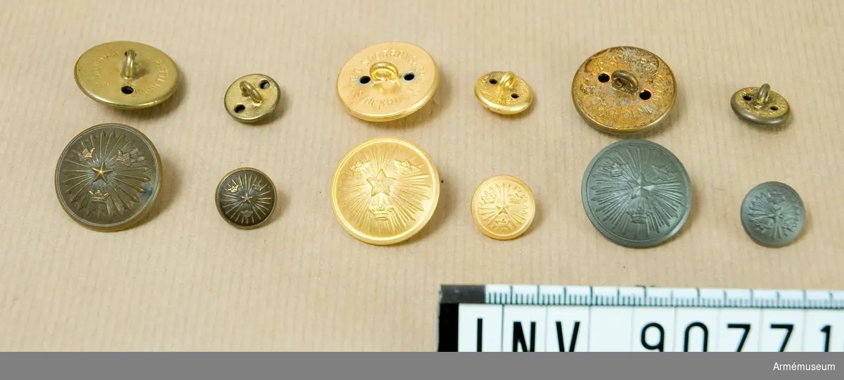 Låda innehållande små och stora knappar i brons och grått. Innehåller även guldfärgade knappar m/1952.